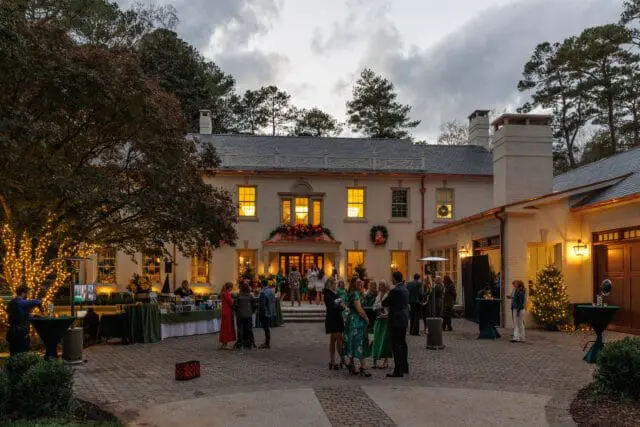 People gathered on a brick patio in front of a light-colored house decorated for the holidays.