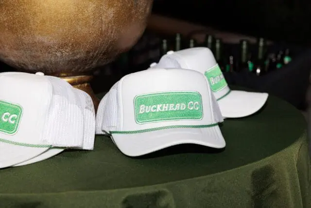 White trucker hats with green 'BUCKHEAD CC' embroidery on a green tablecloth