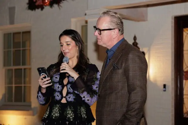 Woman holding a phone and microphone, man in a plaid jacket