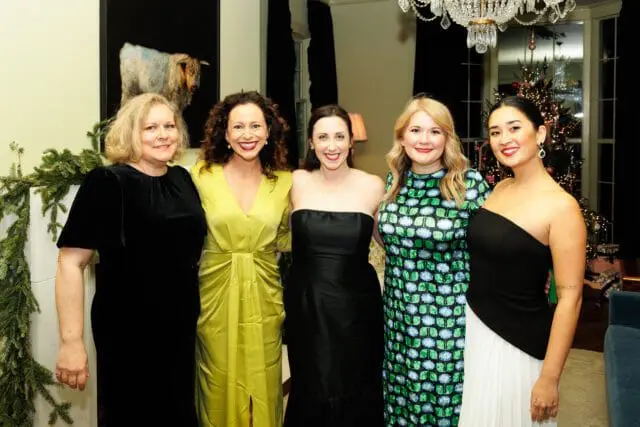 Five women posing in formal attire, with a Christmas tree in the background.