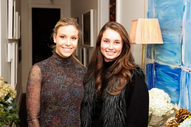 Two women smiling, one in a patterned dress, the other in a fur vest.