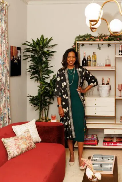 Woman in green dress and floral kimono in a living room with red sofa and bar cart