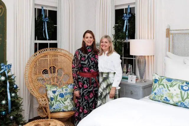 Two women stand in a bedroom decorated for the holidays with wreaths and a Christmas tree.