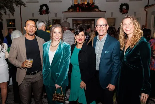 Group of five people posing outdoors in front of a building decorated for the holidays.