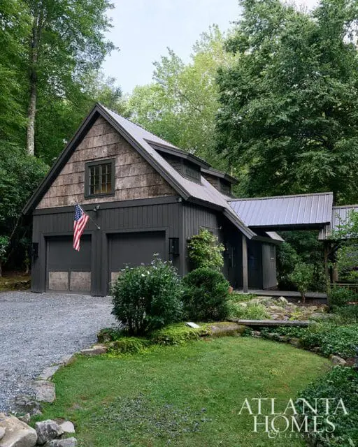 Dark gray garage with wood shingle accents and metal roof, surrounded by trees.