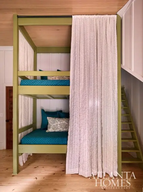 Bunk beds with teal bedding and patterned pillows, green frame, white curtains, and wood floors.
