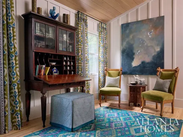 Guest bedroom with antique secretary desk, green velvet chairs, and abstract art.
