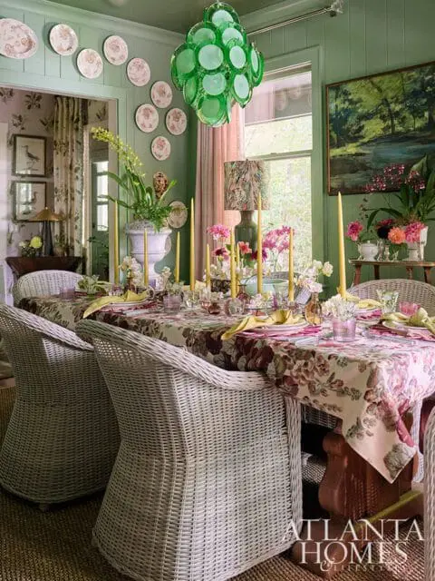 Green dining room with floral tablecloth, wicker chairs, and green chandelier.