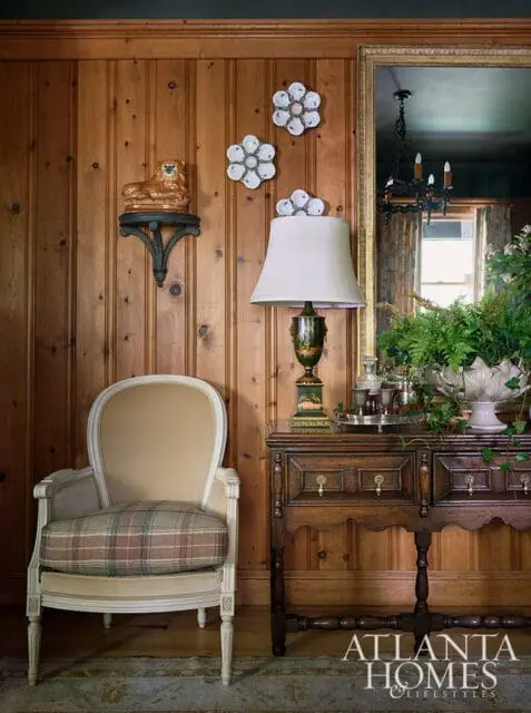 Wood paneled room with upholstered chair, antique desk, and decorative wall art.