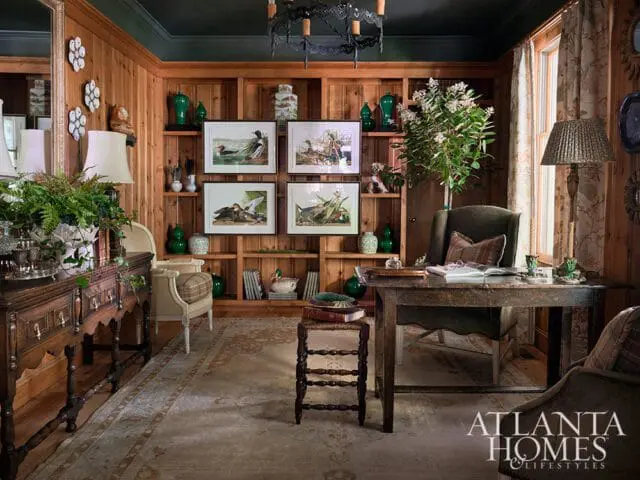Wood paneled study with desk, armchair, and bookshelves displaying artwork and decor.