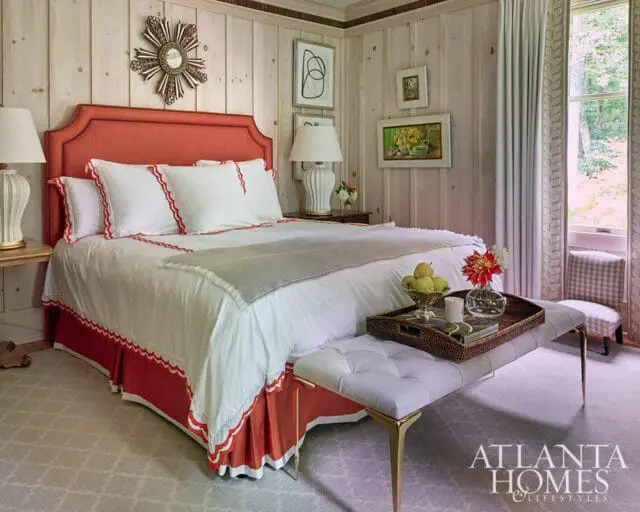 Bedroom with coral headboard, white bedding, wood paneled walls, and a window view
