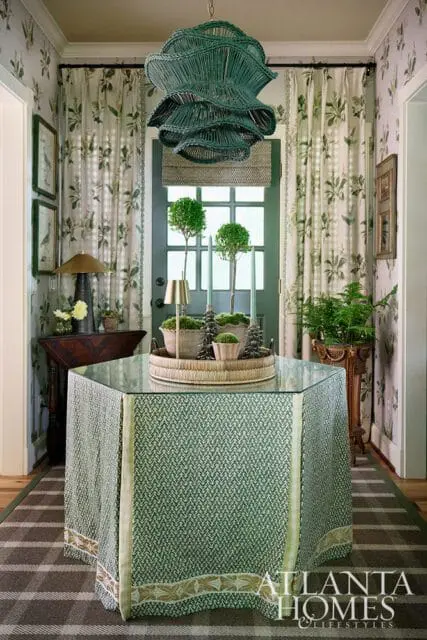 Foyer with green patterned table, wicker chandelier, and botanical print curtains.