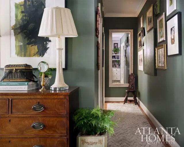 Dark green hallway with antique dresser, lamp, artwork, and mirror