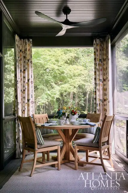 Screened porch with wooden dining set, butterfly curtains, and view of trees