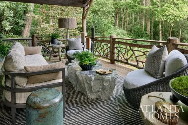 Covered porch with rustic wood railing, stone coffee table, and wicker chairs.