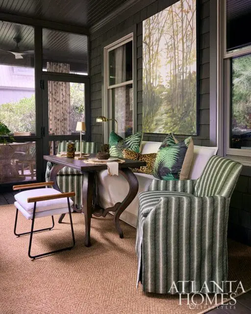 Screened porch with dark wood walls, striped armchair, and botanical art.