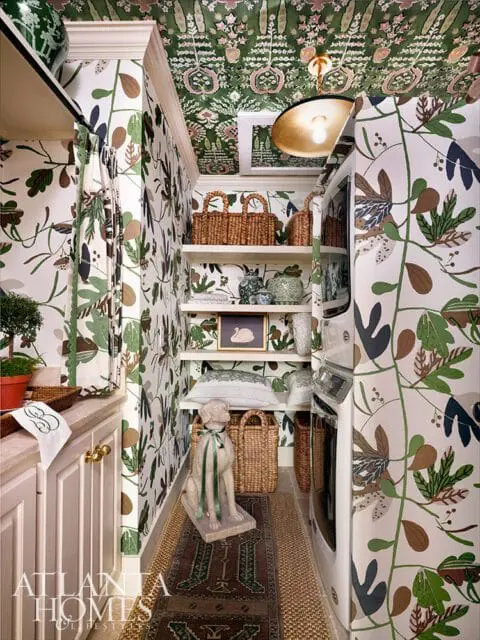 Laundry room with botanical wallpaper, white cabinetry, and stacked washer and dryer.