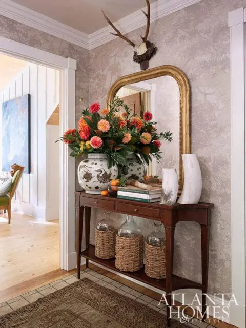 Hallway console table with floral arrangement, mirror, and wicker-wrapped bottles.