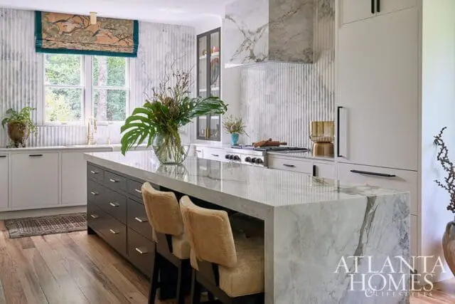 Marble island in modern kitchen with dark wood cabinets and upholstered stools.