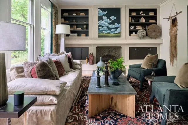 Living room with a large sectional sofa, dark green armchairs, a stone fireplace, and a rug with a