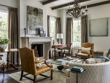 Living room with stone fireplace, leather armchairs, patterned sofa, and dark wood beams.