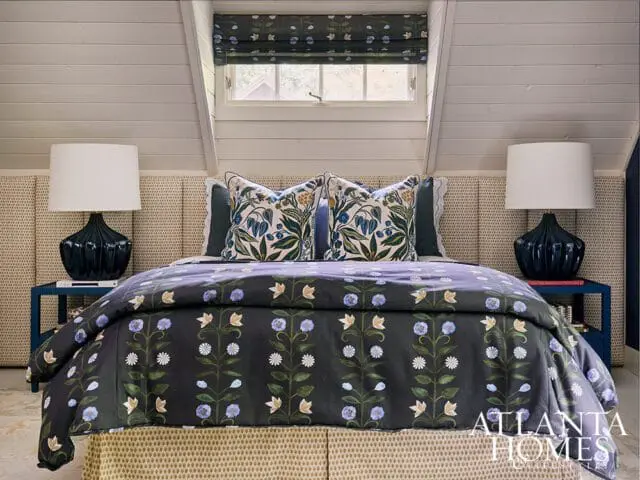 Bedroom with dark floral duvet, patterned headboard, navy lamps, and window with floral shade.