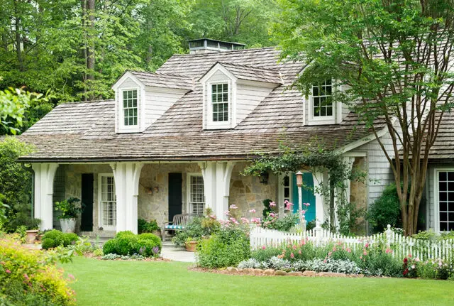 Stone and shingle house with dormer windows, white porch columns, and a turquoise door.
