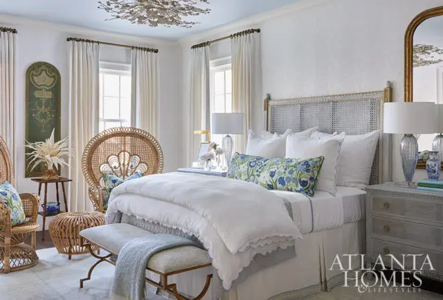Bedroom with white bedding, cane headboard, rattan chairs, and blue floral accents.