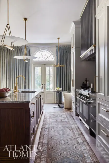 Kitchen with dark wood island, marble countertop, brass faucet, and patterned runner.