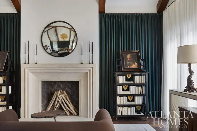 Living room with stone fireplace, dark green curtains, and bookshelf with antique painting.
