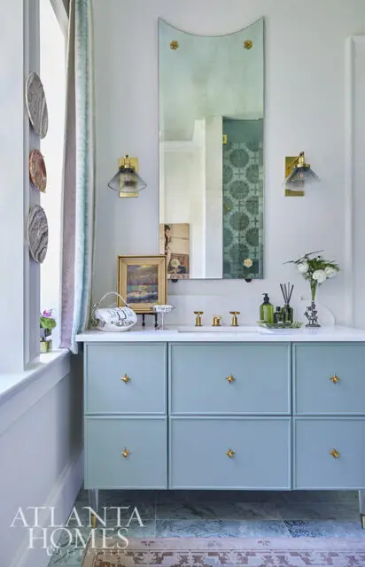 Powder room with light blue vanity, marble countertop, brass fixtures, and ornate mirror.