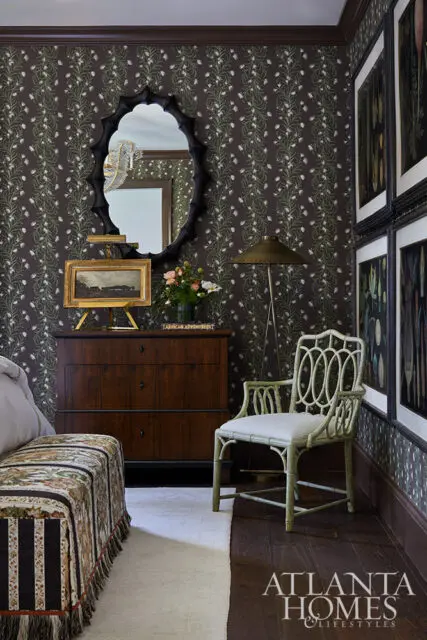 Dark floral wallpaper, dark wood dresser, ornate mirror, and light green chair