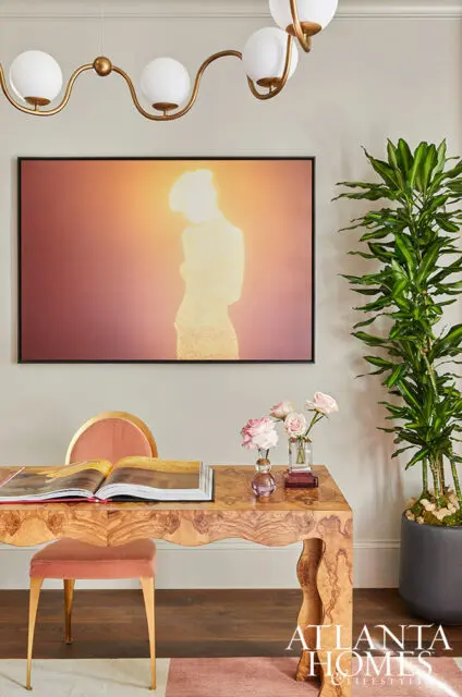 Desk with burl wood finish, open book, pink stool, and artwork of a silhouette.