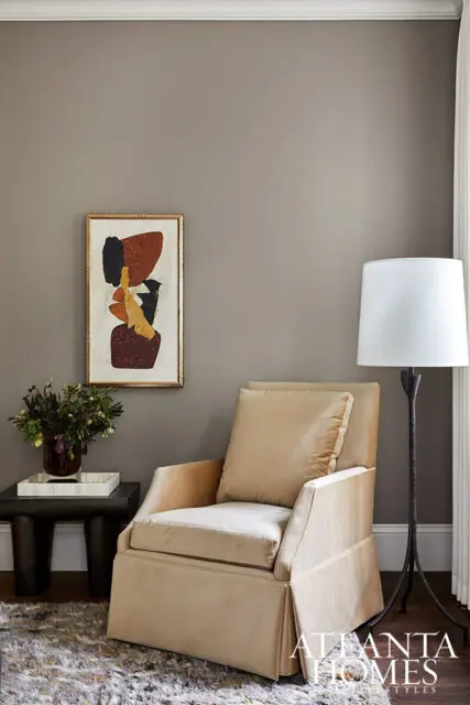 Tan upholstered armchair next to abstract art and a floor lamp.