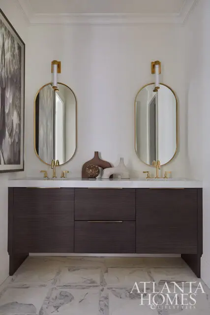 Dark wood vanity with marble countertop, two oval mirrors, and brass fixtures.