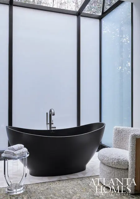 Black freestanding bathtub with chrome faucet, next to a textured armchair.