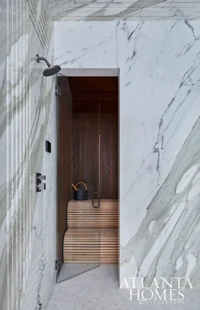 Marble shower with glass door opening to wood-paneled sauna with slatted wooden benches.