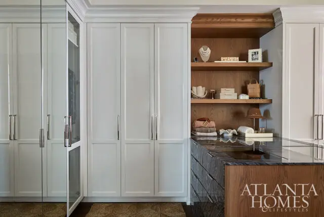 White closet doors with silver handles, wood shelves with accessories, and a marble island.