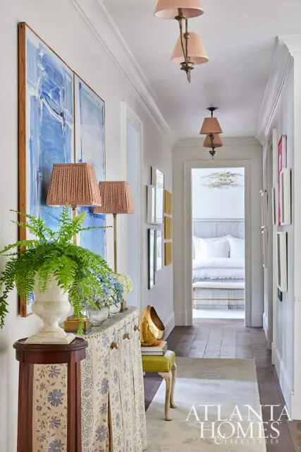 Hallway with abstract blue art, patterned cabinet, and view into a bedroom.