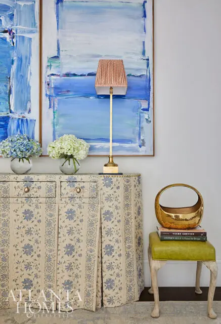Cabinet with blue floral print, brass lamp, and abstract blue paintings