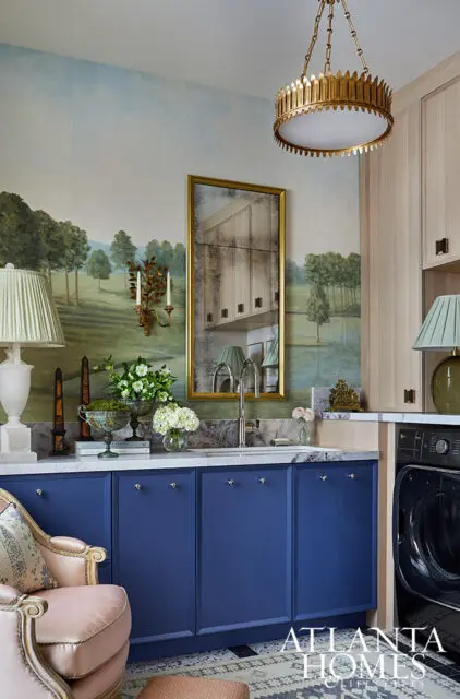 Laundry room with navy blue cabinets, marble countertop, and landscape mural wallpaper.