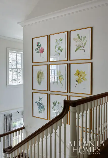 Gallery wall of botanical prints above a staircase with white banister and dark wood handrail.