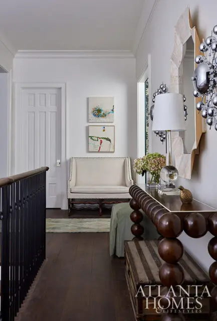 Hallway with white walls, dark wood floors, a white settee, and a console table with a mirrored