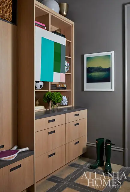 Built-in light wood cabinetry with dark hardware, abstract art, and green boots on patterned floor.
