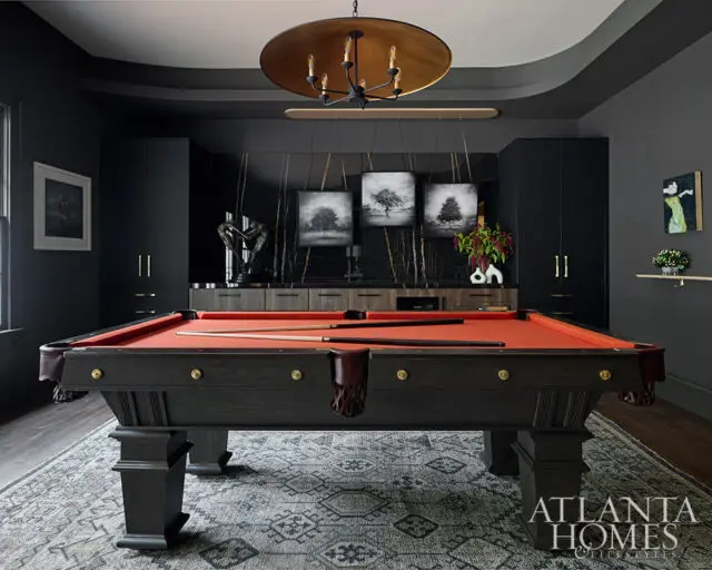 Dark room with a red felt pool table, black cabinetry, and a large gold chandelier.