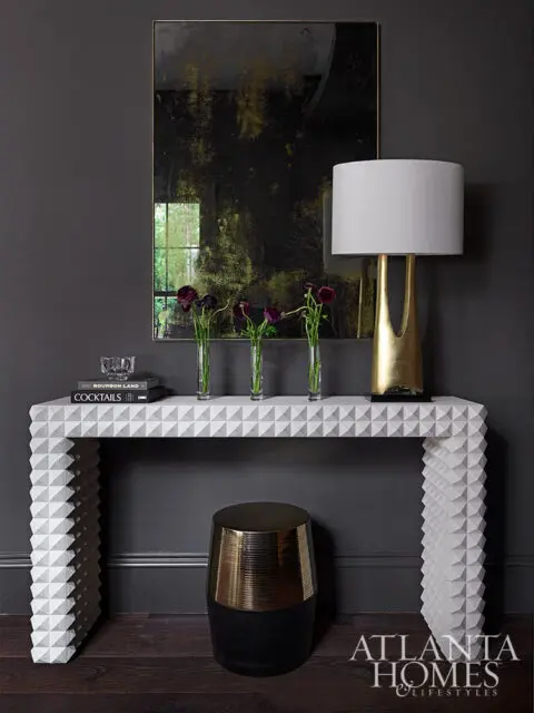 Console table with geometric pattern, gold lamp, and dark flowers.