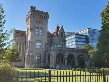 Stone castle with arched entryway and modern glass building behind it.