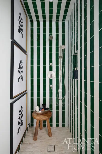 Shower with green and white striped tile, modern chrome fixtures, and botanical art