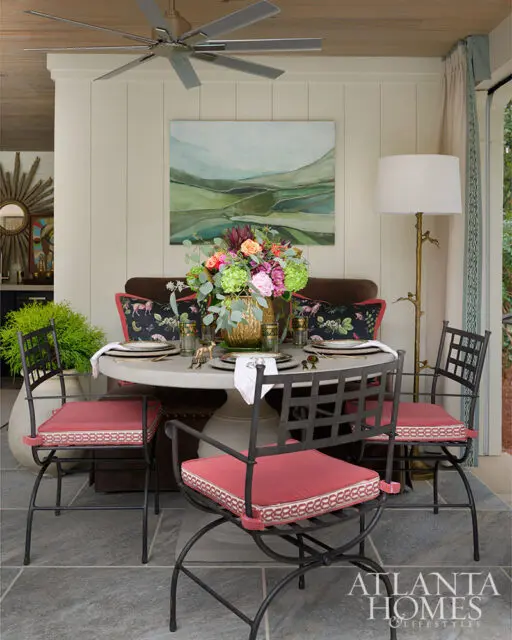 Round dining table with floral centerpiece and four chairs with red cushions.