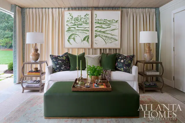 White sofa with green and floral pillows, green ottoman, and two framed green artworks.